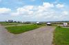 RV Space showing the large, gravel parking area surrounded by grass with views of the beach.